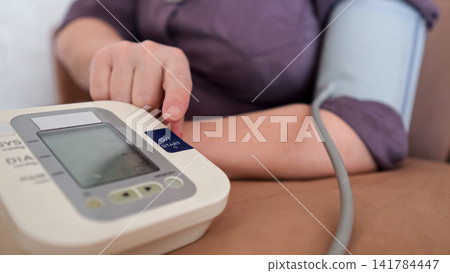 Senior woman checking blood pressure at home with a digital tonometer on her arm, emphasizing self care, prevention, daily monitoring and independent health management Senior woman checking blood pressure at home with a digital tonometer on her arm, emphasizing self care, prevention, daily monitoring and independent health management 141784447