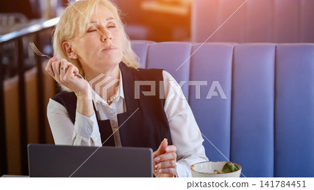 Caucasian Elderly Businesswoman Closing Eyes And Tilting Head Back During Lunch Break, Breathing Deeply In Sunlit Cafe, Serene Expression, Moment Of Stress Relief And Mental Reset Between Meetings. 141784451