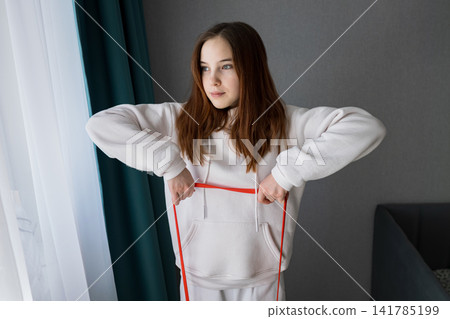 Young woman performing a workout using a red resistance band, focusing on fitness and wellness while staying active and healthy in her comfortable home environment Young woman performing a workout using a red resistance band, focusing on fitness and wellness while staying active and healthy in her comfortable home environment 141785199