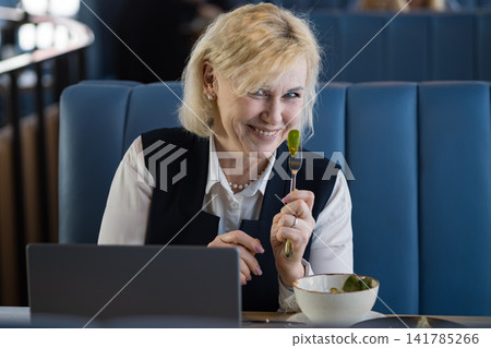 White Consultant Smiling With Salad Fork, Playful Expression In Cozy Cafe Booth With Laptop Nearby, Savoring Fresh Greens And Relaxed Lunch Mood, Mindful Eating And Wellness Focus During Productive 141785266