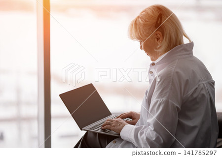 Senior woman focused on her modern laptop keyboard, leveraging technology for remote work and digital literacy from a bright indoor setting with sunlight Senior woman focused on her modern laptop keyboard, leveraging technology for remote work and digital literacy from a bright indoor setting with sunlight 141785297