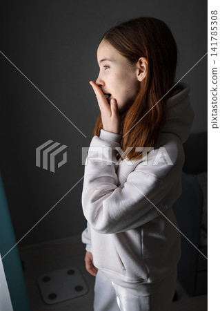 Teen girl yawning and covering her mouth in a cozy hoodie, sleepy and tired in the quiet morning at home, half body profile showing relaxed, natural, candid waking up routine Teen girl yawning and covering her mouth in a cozy hoodie, sleepy and tired in the quiet morning at home, half body profile showing relaxed, natural, candid waking up routine 141785308