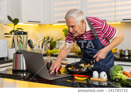 Senior old man cooking healthy vegetables in home kitchen following diet meal recipe on laptop guide Senior old man cooking healthy vegetables in home kitchen following diet meal recipe on laptop guide 141785732