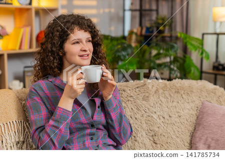 Young woman on home sofa enjoying coffee aroma and quiet break while thinking about new plans calmly Young woman on home sofa enjoying coffee aroma and quiet break while thinking about new plans calmly 141785734