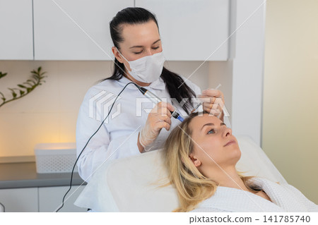Woman receives microneedling and injections for hair growth scalp therapy in trichology clinic Woman receives microneedling and injections for hair growth scalp therapy in trichology clinic 141785740