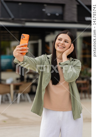 Young woman taking selfie on smartphone walking in city street smiling and checking portrait frame Young woman taking selfie on smartphone walking in city street smiling and checking portrait frame 141785741