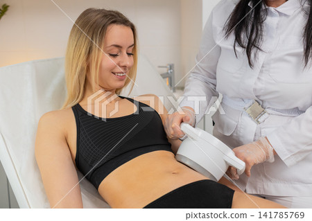 Woman receiving LPG vacuum massage on belly area by cosmetologist using modern equipment in clinic Woman receiving LPG vacuum massage on belly area by cosmetologist using modern equipment in clinic 141785769