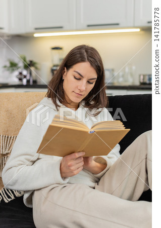 Young woman enjoys leisure reading paper book smiles in comfort turns pages with bookmark calm ease Young woman enjoys leisure reading paper book smiles in comfort turns pages with bookmark calm ease 141785778