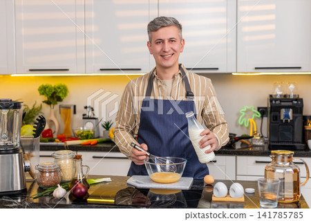 Middle-aged man whisking eggs with milk in kitchen for homemade breakfast meal and morning routine Middle-aged man whisking eggs with milk in kitchen for homemade breakfast meal and morning routine 141785785