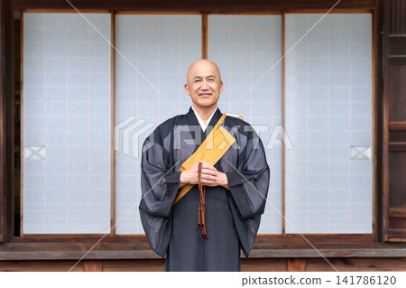 A monk stands in front of the main hall of a temple, holding prayer beads. A monk stands in front of the main hall of a temple, holding prayer beads. 141786120