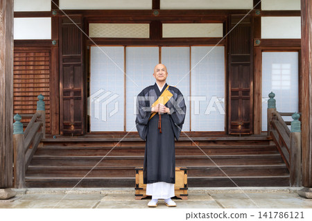 一位僧人站在寺廟大殿前,手持念珠。 一位僧人站在寺廟大殿前,手持念珠。 141786121