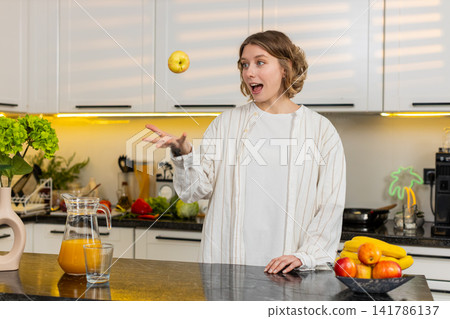 Young woman tossing apple in kitchen during healthy breakfast break with playful smile for diet plan Young woman tossing apple in kitchen during healthy breakfast break with playful smile for diet plan 141786137