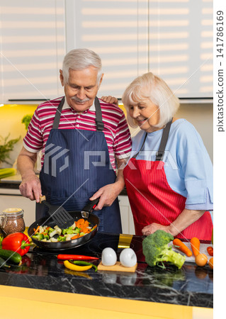 Senior old woman man cooking vegetable stir fry in home kitchen for healthy diet nutrition lifestyle Senior old woman man cooking vegetable stir fry in home kitchen for healthy diet nutrition lifestyle 141786169
