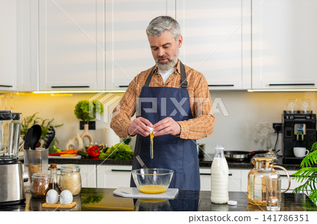 Middle-aged man smiling cracking eggs whisking mixture in home kitchen for diet nutrition meal prep Middle-aged man smiling cracking eggs whisking mixture in home kitchen for diet nutrition meal prep 141786351