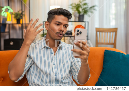 Indian man on video chat with friend laughs waves hello goodbye shows ok sign during chat smiles fun 141786437