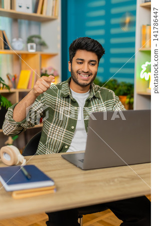Indian man on home table explaining business idea on laptop video call with confident smile for work 141786447