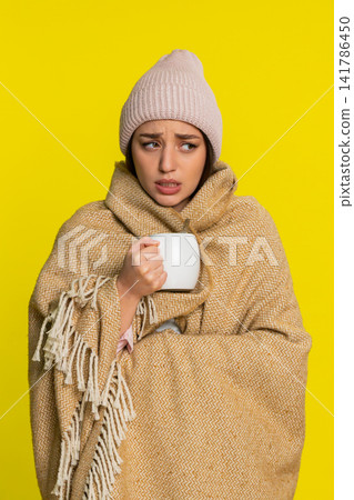 Woman wrapped in blanket wearing hat adding honey to tea slowly drinking caring for sore throat Woman wrapped in blanket wearing hat adding honey to tea slowly drinking caring for sore throat 141786450