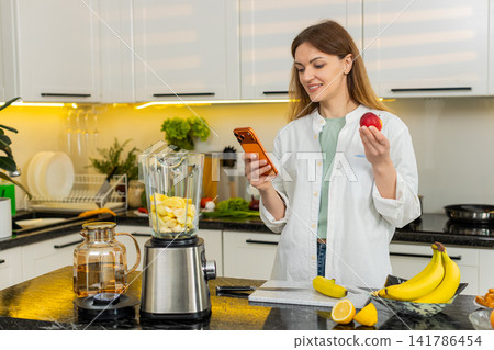 Middle-aged woman choosing fruit for smoothie using smartphone in home kitchen for healthy diet plan Middle-aged woman choosing fruit for smoothie using smartphone in home kitchen for healthy diet plan 141786454