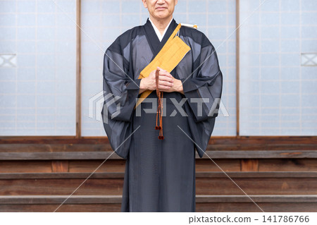 一位僧人站在寺廟大殿前,手中拿著念珠。 一位僧人站在寺廟大殿前,手中拿著念珠。 141786766