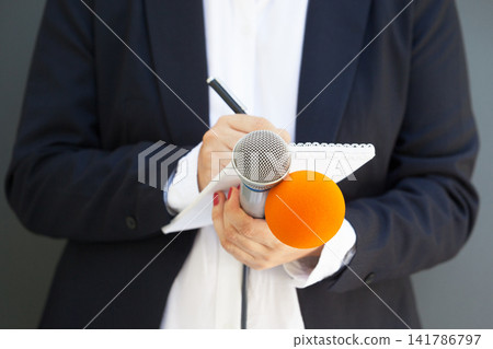Female journalist at news conference or media event, writing notes, holding microphone Female journalist at news conference or media event, writing notes, holding microphone 141786797