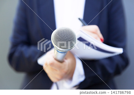 Female journalist at news conference or media event, writing notes, holding microphone Female journalist at news conference or media event, writing notes, holding microphone 141786798