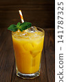 Orange juice in glass with ice cubes, fresh mint sprigs and striped straw on dark wooden table 141787325