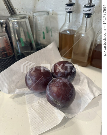 Ripe, deep purple plum with a dusty bloom, sliced open to reveal its juicy amber flesh. Isolated on a dark background for fresh food and healthy eating concepts. Ripe, deep purple plum with a dusty bloom, sliced open to reveal its juicy amber flesh. Isolated on a dark background for fresh food and healthy eating concepts. 141787694