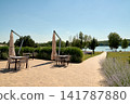 A vacation resort with an open-air terrace featuring tables and umbrellas, offering a view of a tranquil lake. 141787880