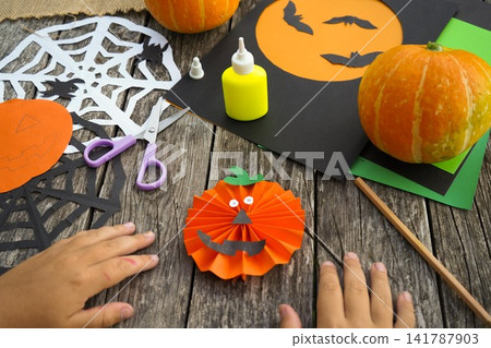 Close up of kids hands gluing googly eyes onto a handmade paper jack-o'-lantern face detail Close up of kids hands gluing googly eyes onto a handmade paper jack-o'-lantern face detail 141787903