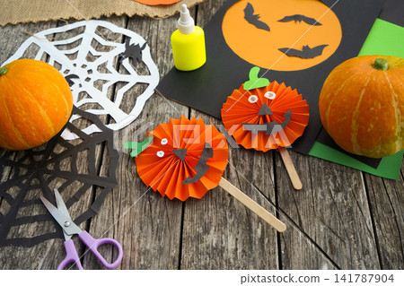 High angle shot of two finished handmade paper pumpkin crafts on sticks with holiday decorations High angle shot of two finished handmade paper pumpkin crafts on sticks with holiday decorations 141787904