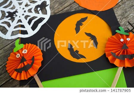 Spooky holiday craft mockup featuring handmade paper jack-o'-lanterns, paper bats and a cutout moon Spooky holiday craft mockup featuring handmade paper jack-o'-lanterns, paper bats and a cutout moon 141787905