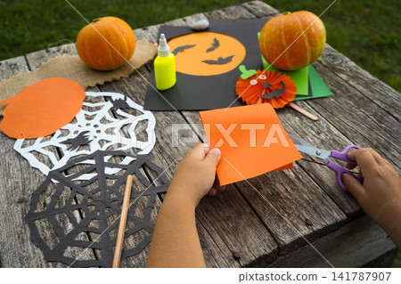 Over the shoulder shot of children hands choosing orange and green paper for making a handmade pumpkin Over the shoulder shot of children hands choosing orange and green paper for making a handmade pumpkin 141787907