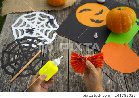 Detailed shot of a child hand gluing an accordion folded paper element for a DIY holiday decoration project Detailed shot of a child hand gluing an accordion folded paper element for a DIY holiday decoration project 141788025