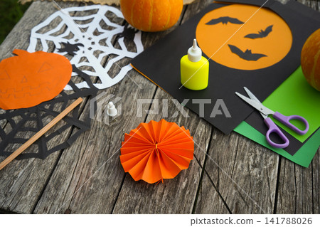 Spooky holiday craft mockup with a handmade pleated paper element, paper silhouettes and scissors outdoors Spooky holiday craft mockup with a handmade pleated paper element, paper silhouettes and scissors outdoors 141788026