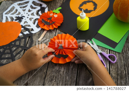Little girl applying paper cutouts onto a wooden stick to make a creative Halloween pumpkin prop Little girl applying paper cutouts onto a wooden stick to make a creative Halloween pumpkin prop 141788027