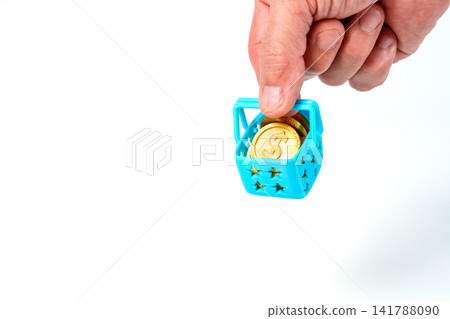 Hand holding a miniature blue shopping basket filled with gold dollar coins on white background. Professional close up representing inflation, consumer spending, retail costs and personal finance. Hand holding a miniature blue shopping basket filled with gold dollar coins on white background. Professional close up representing inflation, consumer spending, retail costs and personal finance. 141788090