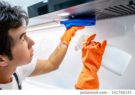Asian man housekeeper holding spray bottle while wiping microfiber cloth on cooker hood Asian man housekeeper holding spray bottle while wiping microfiber cloth on cooker hood 141788141