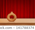 A modern-style terracotta vase sits on a wooden table against a red curtain backdrop. 141788374