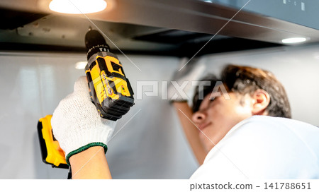 Asian male technician using electric screwdriver fixing extractor motor in cooker hood Asian male technician using electric screwdriver fixing extractor motor in cooker hood 141788651