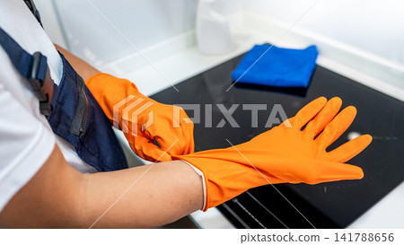 Worker hand putting on orange rubber gloves Worker hand putting on orange rubber gloves 141788656