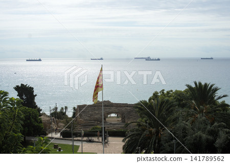The Roman amphitheatre of Tarragona by the sea with a Catalan flag and cargo ships. Ancient Roman ruins in Catalonia The Roman amphitheatre of Tarragona by the sea with a Catalan flag and cargo ships. Ancient Roman ruins in Catalonia 141789562