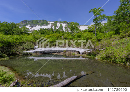 A breathtaking early summer scene in Hokkaido's Daisetsuzan Mountains, featuring Kamo-numa Pond in the Daisetsu Plateau and lingering snow. A breathtaking early summer scene in Hokkaido's Daisetsuzan Mountains, featuring Kamo-numa Pond in the Daisetsu Plateau and lingering snow. 141789690