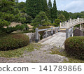 A dignified Japanese landscape created by beautifully pruned pine trees and an arched bridge crossing a pond. 141789866