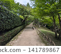 A quiet path through a Japanese-style garden, bathed in lush greenery and dappled sunlight. 141789867