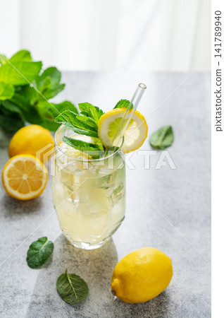 A summer drink with lemon, mint, and ice in a two glasses against a sunny window background. A summer drink with lemon, mint, and ice in a two glasses against a sunny window background. 141789940