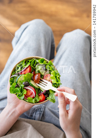 A woman holds a healthy vegetable salad in an eco-friendly takeaway bowl. A woman holds a healthy vegetable salad in an eco-friendly takeaway bowl. 141789942