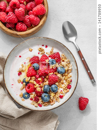 Natural yogurt with granola, blueberry and raspberry in a bowl on a light concrete background Natural yogurt with granola, blueberry and raspberry in a bowl on a light concrete background 141789950