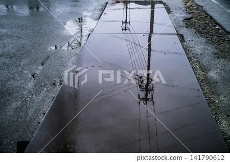 The scenery of utility poles and power lines reflected on the surface of the rain-soaked steel plates. The scenery of utility poles and power lines reflected on the surface of the rain-soaked steel plates. 141790612