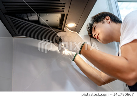 Asian male technician removing range metal filter looking at extractor motor inside the cooker hood Asian male technician removing range metal filter looking at extractor motor inside the cooker hood 141790667