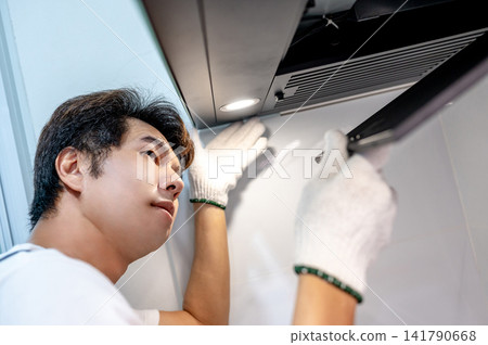 Asian male technician removing range metal filter looking inside the cooker hood Asian male technician removing range metal filter looking inside the cooker hood 141790668